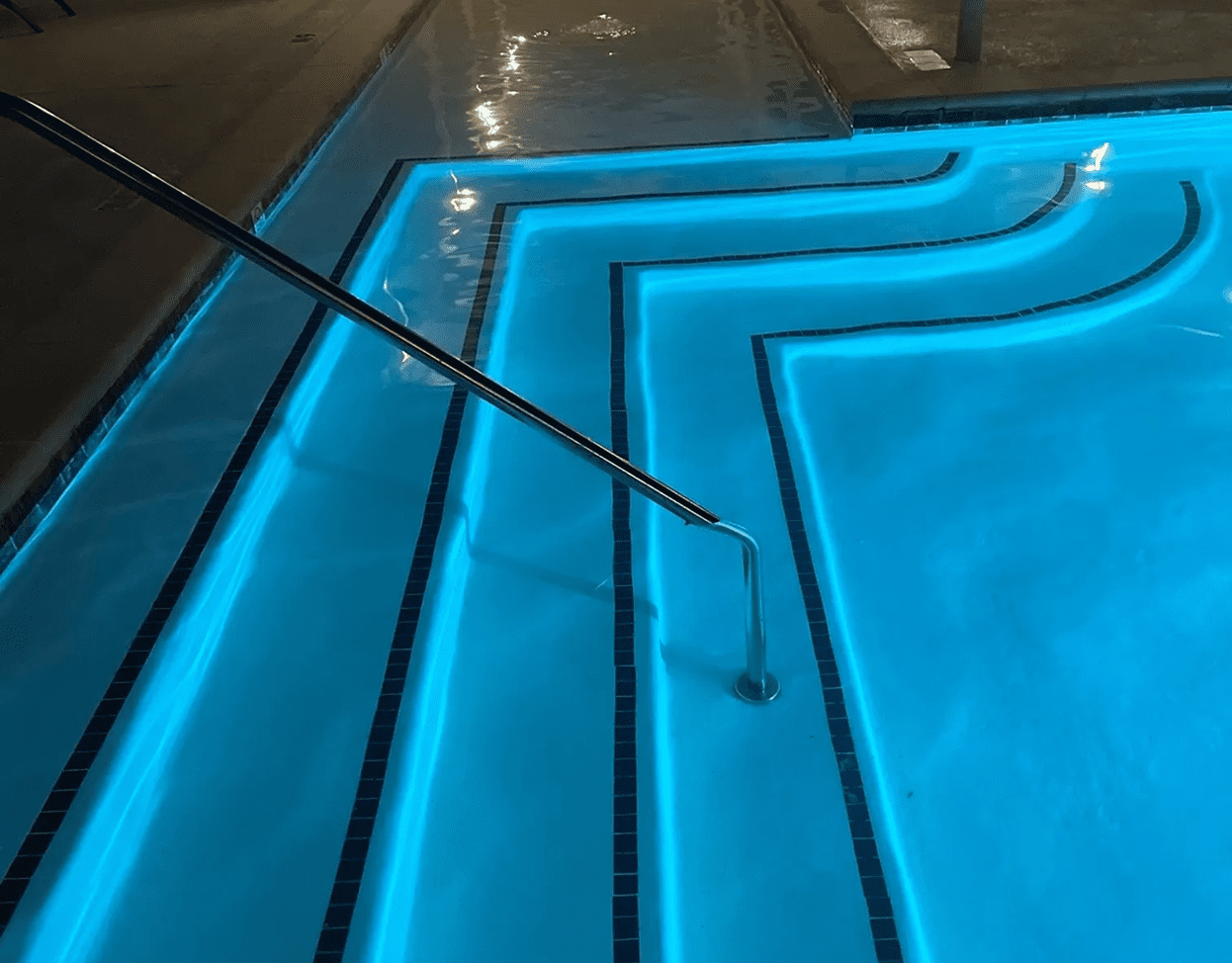 Illuminated swimming pool with metal handrail.