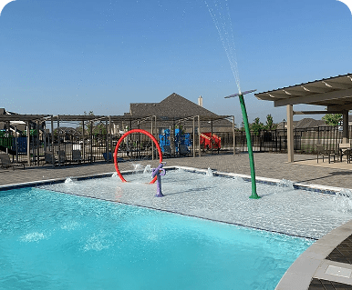 A sunny outdoor pool with water play structures and a pergola.