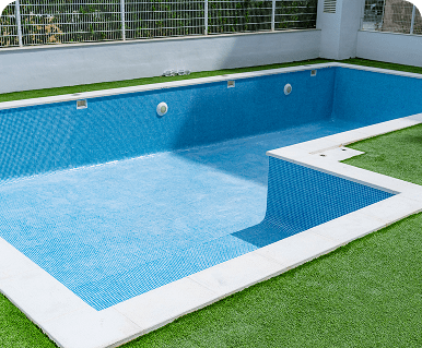 Empty blue swimming pool with artificial grass around.