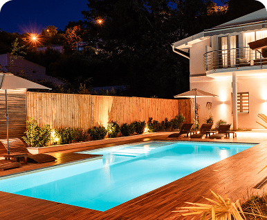 Illuminated backyard pool at night with modern lighting and wooden deck.